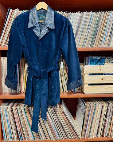 Blue velvet jacket with a collar on a hanger against a background of records and books.